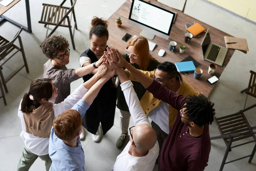 Em um escritório, um grupo de pessoas comemorando, com as mãos levantadas, demonstrando entusiasmo e trabalho em equipe.