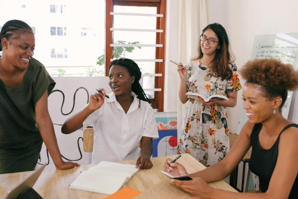 Quatro mulheres sorrindo em uma foto enquanto estão trabalhando.