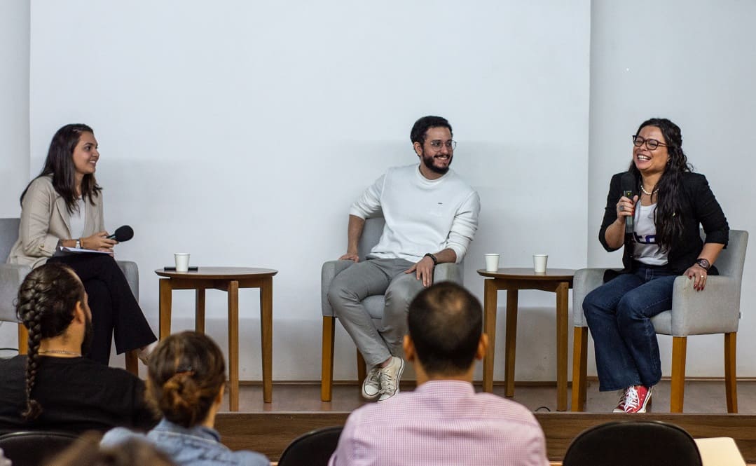 Três profissionais no palco, sorrindo e interagindo com o público durante uma palestra