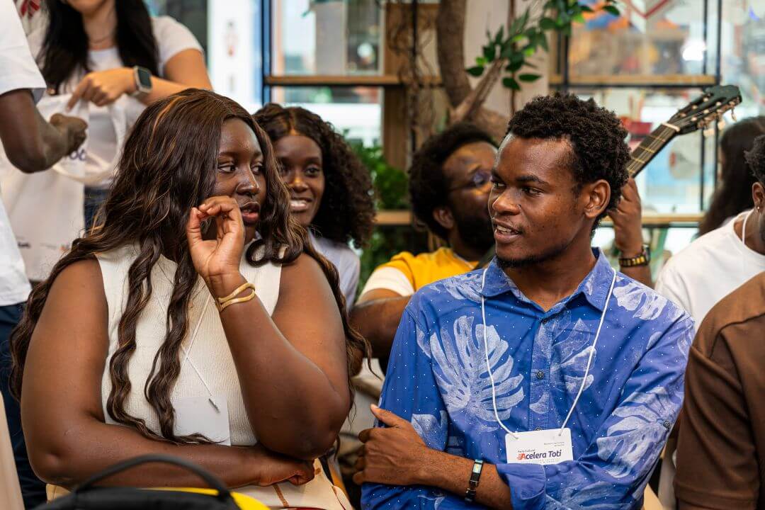 Grupo de pessoas sentadas, com destaque para duas sentadas a frente conversando.