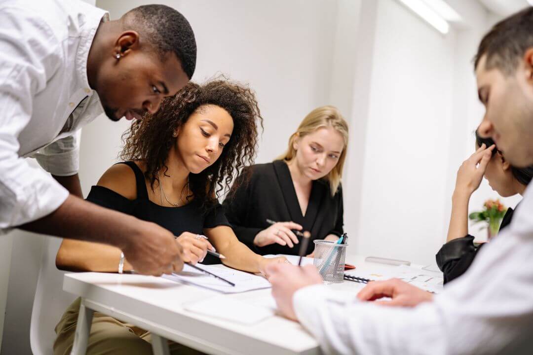 Grupo de pessoas sentadas à mesa analisando trabalhos