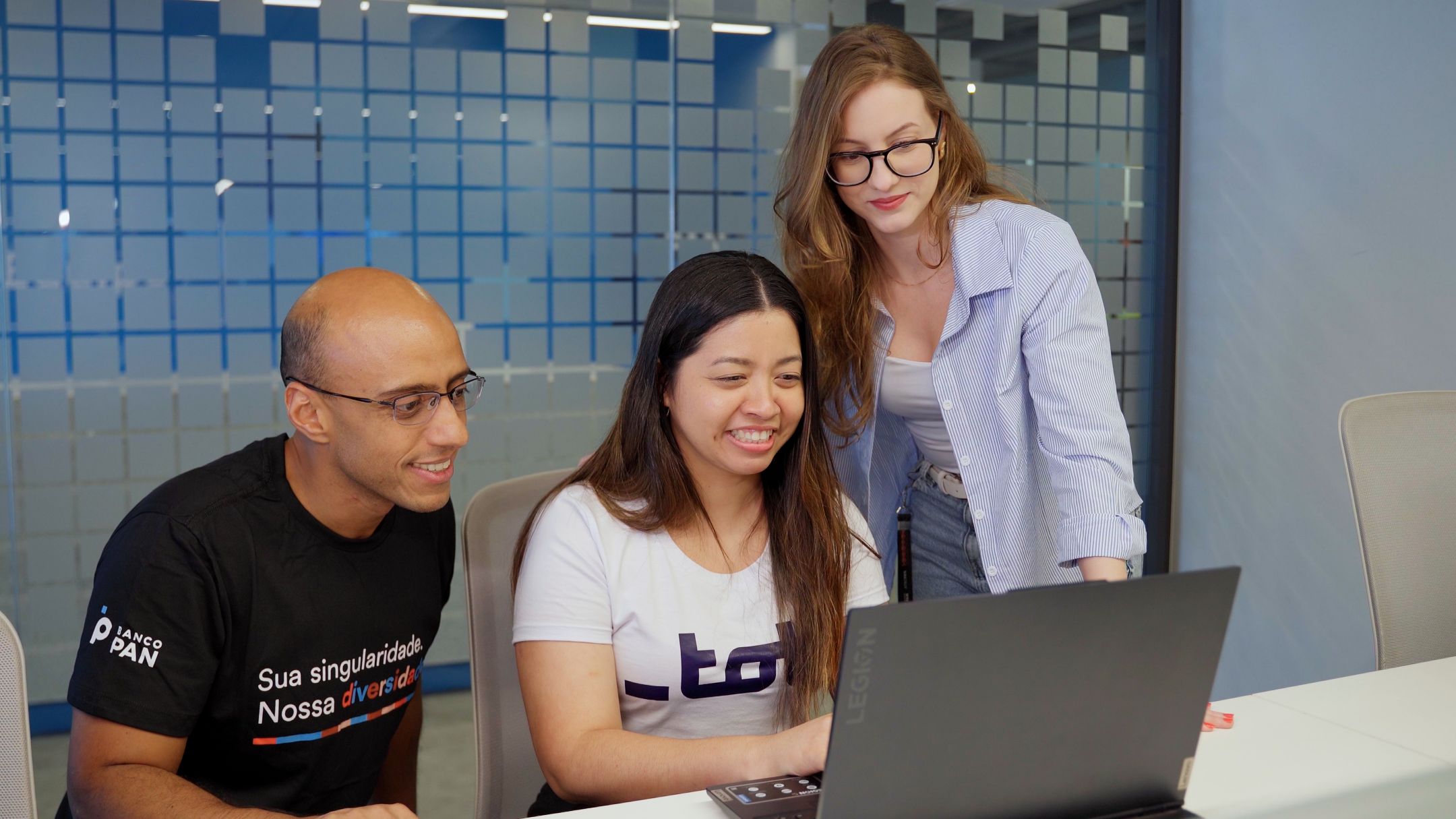 Três pessoas sorrindo em frente ao computador durante projeto de formação profissional da Toti em parceria com o Banco PAN